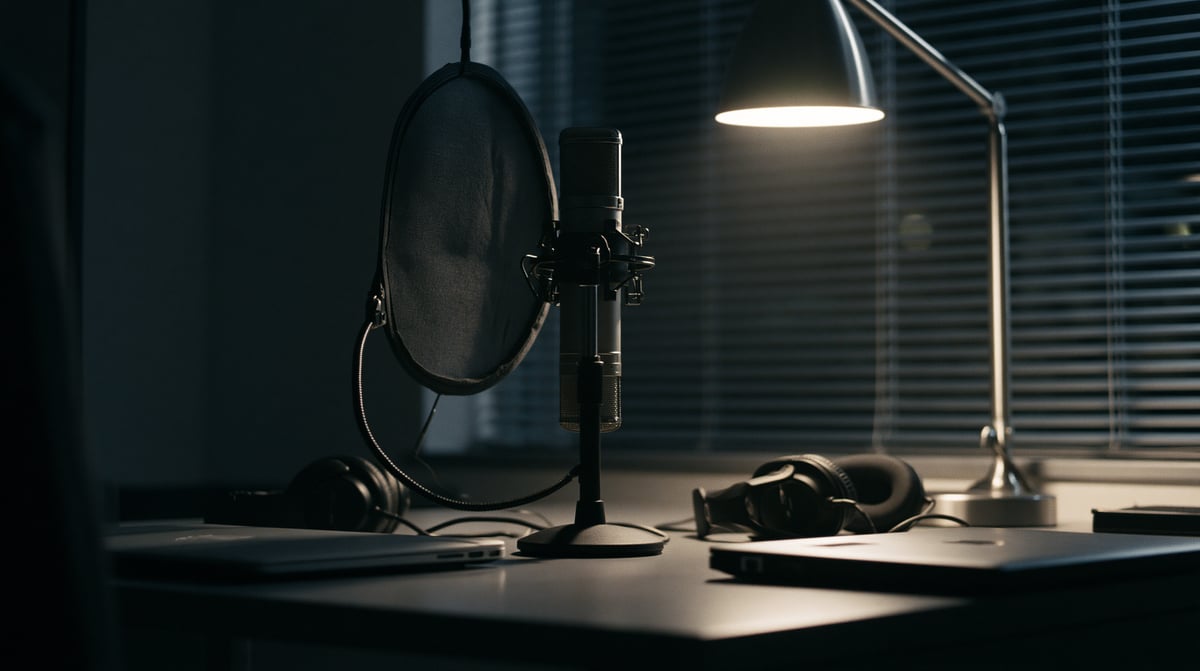 A condenser microphone with a reflection filter, headphones and a lamp on a desk.