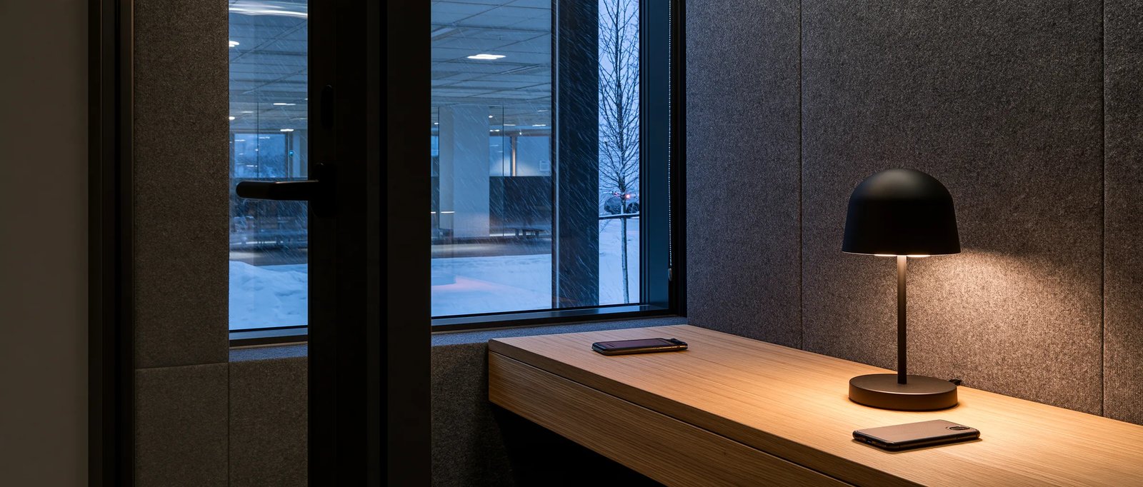 An empty voice recording booth in an office at dusk, a phone on the ledge under one lamp.