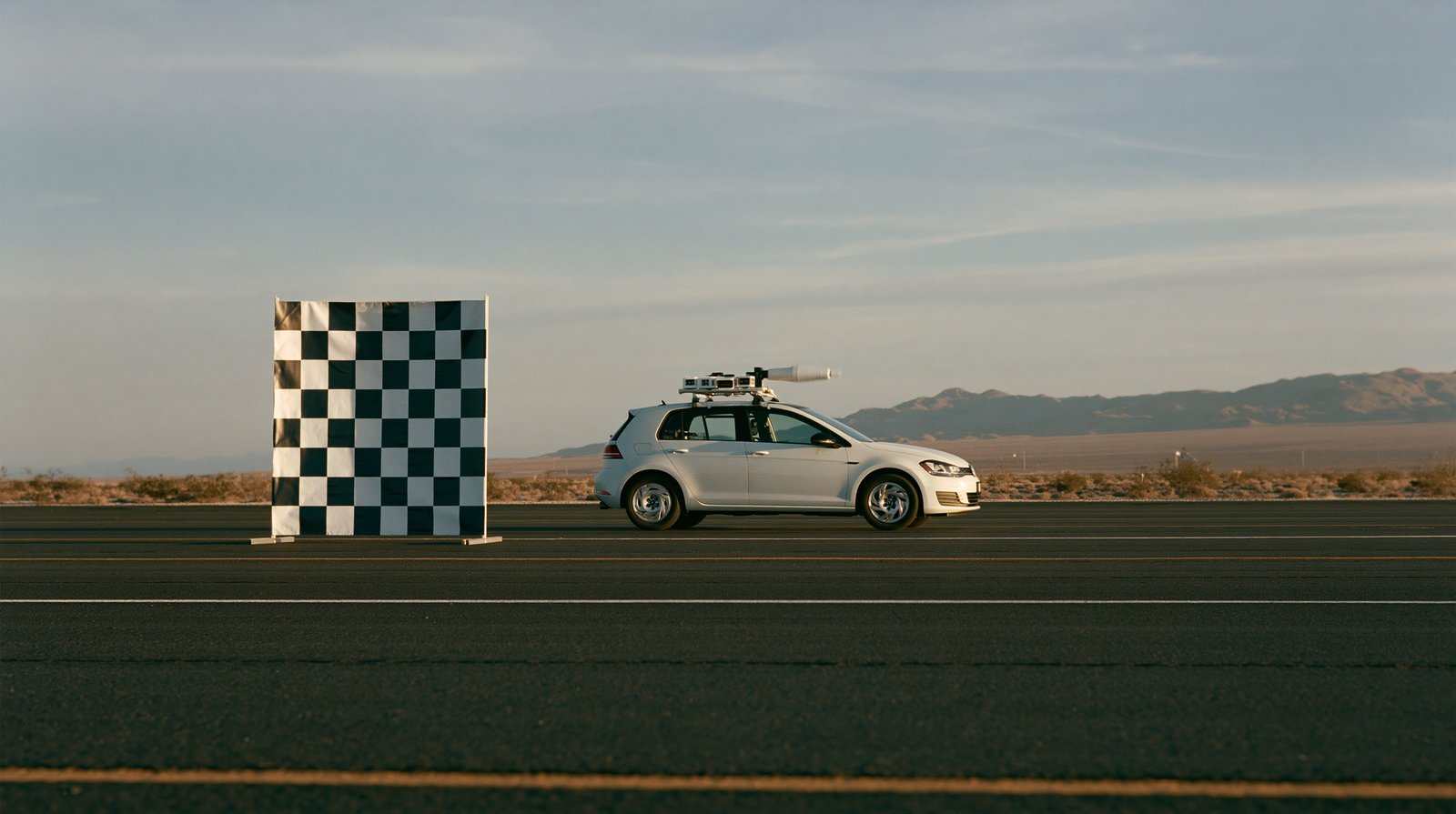 White hatchback with a roof sensor rack and a standing checkerboard calibration target.
