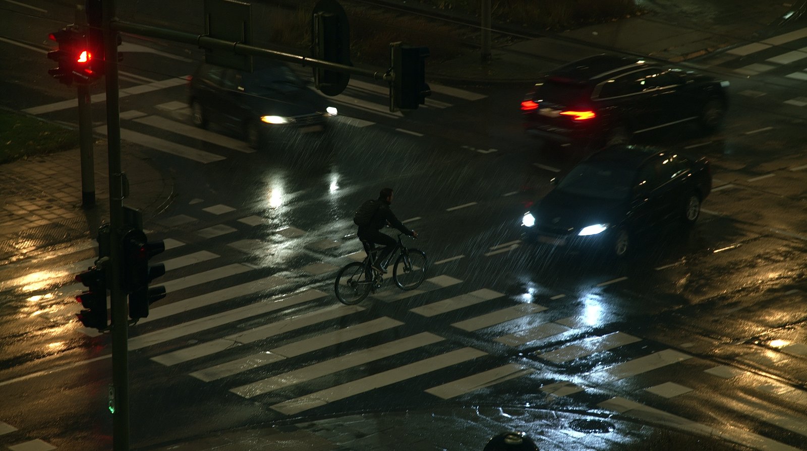 Wet city intersection at night with a cyclist and cars.