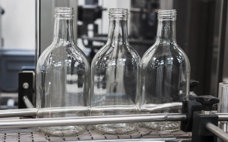 Clear glass bottles on a production line, their outlines almost indistinguishable from the background
